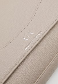 Bežová texturovaná kožená peněženka s embosovaným nápisem "AIX" a "ARMANI EXCHANGE" v lesklém stříbrném provedení, s jemným prošíváním a elegantním designem.