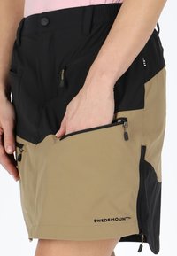Two-tone shorts in black and tan fabric, featuring multiple zippered pockets, a slim fit, and visible brand logo, designed for functionality.