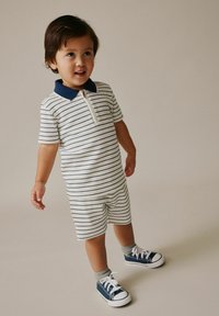 Stribet kortærmet polo-romper med navy krave, inkluderer en halv lynlås og matchende shorts. Kompletteres med blå sneakers og grå sokker.