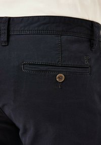 Dunkelblaue Hose mit einer Gesäßtasche mit Knopfschluss und kontrastierenden Nähten. Das Material wirkt glatt und robust.