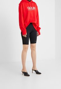 Punainen huppari valkoisella logolla, yhdistetty mustiin pyöräilijöiden shortseihin, joissa on sivukoristukset. Yhdistetty mustiin mooli-saappaisiin. Yksinkertainen, rento asu.