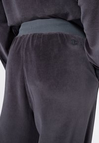 Graue Velours-Sweatpants mit einem gerippten Bund. Enthält ein dezentes Logo-Detail auf der Rückseite, das die glatte Textur und die maßgeschneiderte Passform präsentiert.