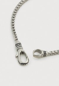 Ασημένιο βραχιόλι αλυσίδα με κούμπωμα και διακοσμητικές λεπτομέρειες. Διαθέτει στριφτό σχέδιο και στρογγυλές χάντρες κοντά στο κούμπωμα.