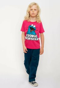 Pink cotton t-shirt featuring a blue Cookie Monster graphic, paired with navy sweatpants and black canvas shoes with white soles.