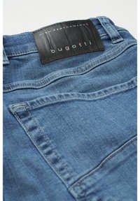 Niebieskie dżinsy denimowe z czarną skórzaną metką na pasku, z delikatnymi detalami w szyciu i klasycznym pięciokomorowym fasonem.