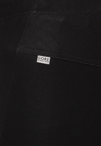 Schwarze Stretch-Laufshorts aus einem glatten Material mit einem sichtbaren Etikett, auf dem "GORE RUNNING WEAR" im Rückentasche steht.