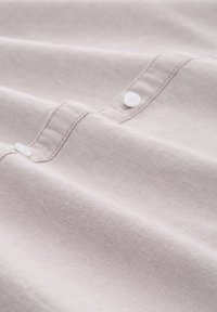 Licht taupe stof met een gladde textuur, met knopen op een pat. De stof lijkt enigszins gekreukt met subtiele stikdetails.