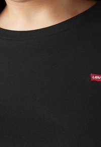 Mustan puuvillaisen t-paidan ribbauskaulus ja pieni punainen Levi's-logo vasemmassa rinnassa. Suora tekstuuri, yksinkertainen muotoilu.