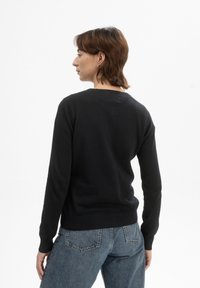 Zwarte gebreide trui met lange mouwen, geribde manchetten en zoom. Gekocht met lichtblauwe denim jeans. Zachte textuur, klassieke ronde hals.