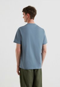 T-shirt a maniche corte in cotone azzurro chiaro, con scollatura rotonda e un design semplice, abbinato a pantaloni larghi verde oliva.