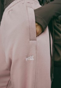 Pehmed roosad dressipüksid küljetaskuga, elastse vöökoha ja alumises sääres valge tikandiga "self." logo. Sile, tekstuuriga kangas.