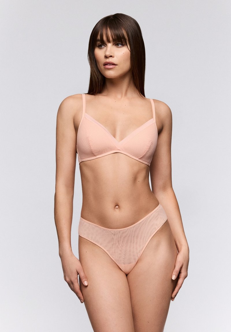 Lichtroze bh en hooggeknipte slipset gemaakt van doorzichtig geribbeld materiaal, met verstelbare bandjes en een gladde textuur. Eenvoudig ontwerp in het algemeen.