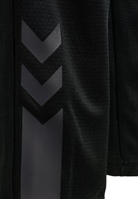Schwarze Sportjacke aus strukturiertem Material, mit glänzenden Chevron-Mustern an der Seite für zusätzlichen Designdetails.