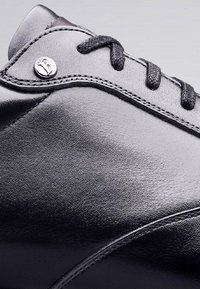 Zwarte leren schoen met een gladde textuur, met een ronde neus, metalen accenten en gestikte details langs de bovenkant en het vetersluitinggebied.