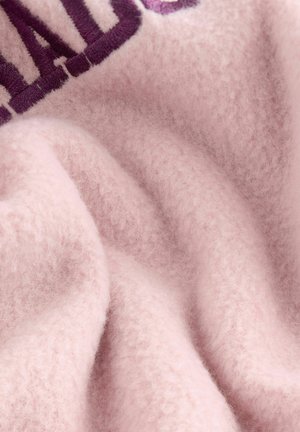 Vaaleanpunainen fleece-kangas, jossa on pehmeä ja pörröinen pinta, ja tumman violetilla ommeltu kuvio. Materiaali vaikuttaa paksulta ja mukavalta.