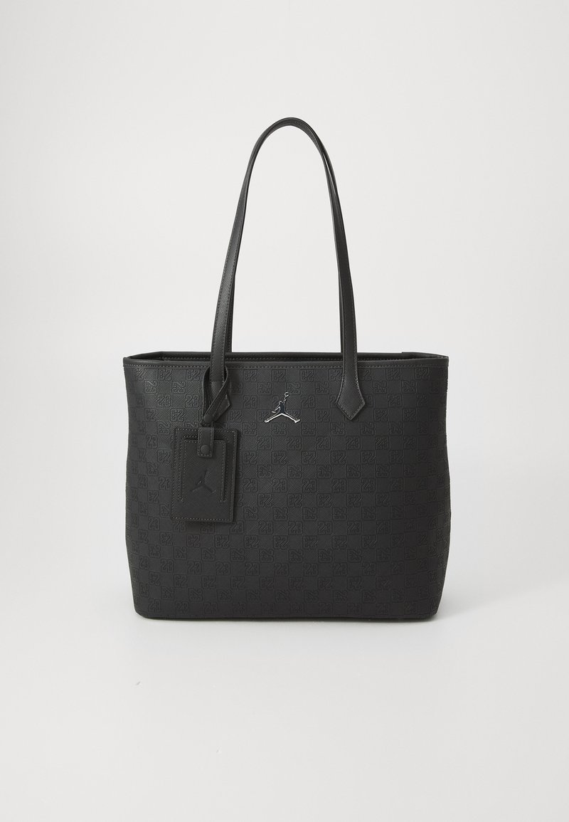 Svart totebag med preget mønster, to lange håndtak, rektangulær form og et klistremerke med logodetalj. Laget av slitesterkt materiale.