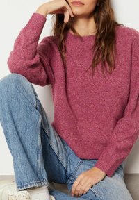 Pull en tricot fuchsia avec un motif en losange et des poignets côtelés, assorti à un jean bleu clair ample et des baskets blanches.