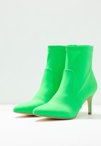 Zelené kotníkové boty vyrobené z hladkého, elastického materiálu s špičatou špičkou a štíhlými podpatky. Mají bezešvý design a minimální švy.