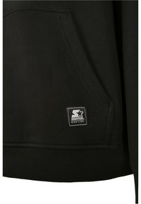 Svart sweatshirt med kengurulomme, ribbet hem og teksturert stoff. Inkluderer et svart-hvitt "Starter Black Label" logo-patch.