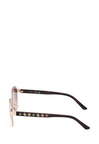 Zonnebril met een slank gouden metalen frame, gradient glazen en boekhoutkleurige pootjes met decoratieve gouden motieven.