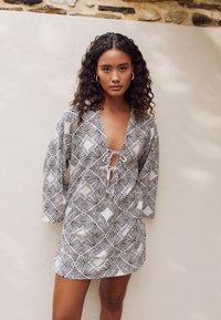 Short dress in black and white patterned fabric featuring a deep V-neck, tie closure, and three-quarter sleeves with a loose fit.