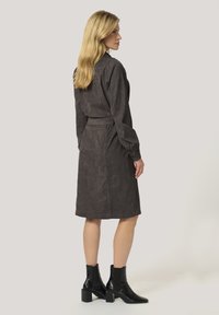 Donkergrijze, gestructureerde jurk met lange mouwen, een ceintuur in de taille en een middellange snit, gecombineerd met zwarte enkellaarsjes en een gladde afwerking.