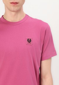 Ροζ βαμβακερό T-shirt με στρογγυλή λαιμόκοψη και κοντά μανίκια. Διαθέτει μία μαύρη ετικέτα με λογότυπο στο αριστερό στήθος με σχέδιο φτερού.