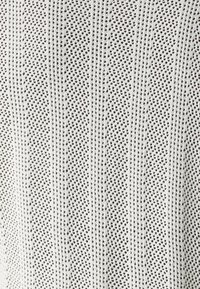 Tejido de punto con una trama abierta y franjas verticales alternas; predominantemente blanco con pequeños puntos negros; ligero y texturizado.