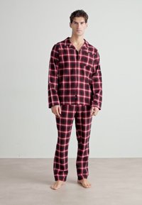 Röd och svart rutigt flanellpyjamas-set med långa ärmar och byxor, som har en knappad skjorta och en avslappnad passform. Mjuk textur med synliga rutor.