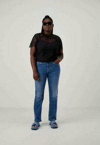 Svart topp med blondekanter, blå jeans og blå sandaler. Toppen har korte ermer og diskrete blondedetaljer, mens jeansene er tettsittende.