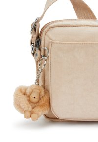 Beige fabric bag with a textured finish, featuring a zipper and a side pocket. Attached is a fluffy charm resembling a monkey.