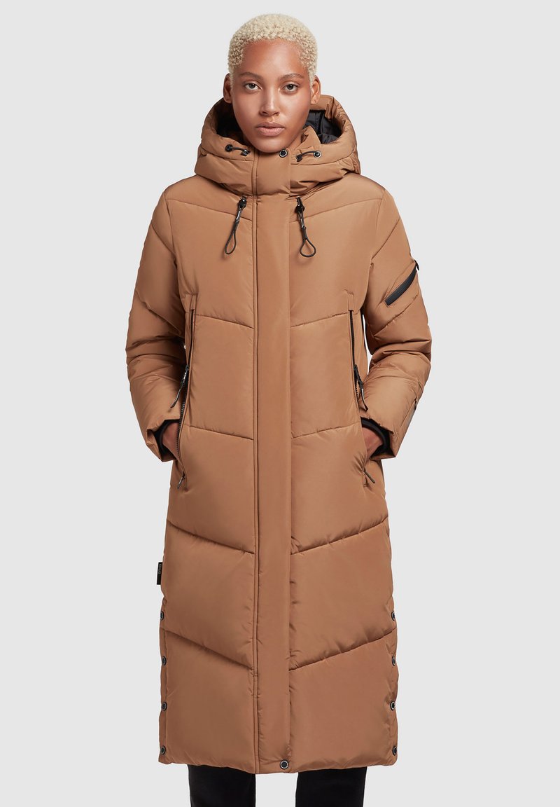 Abrigo acolchado largo marrón con capucha, que presenta paneles acolchados verticales, cordones ajustables y bolsillos con cremallera. Textura suave y diseño hasta la rodilla.