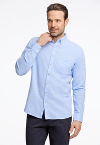 Lichtblauwe overhemdbloes met een puntige kraag, lange mouwen en een borstzak, gemaakt van een gevarieerde stof.