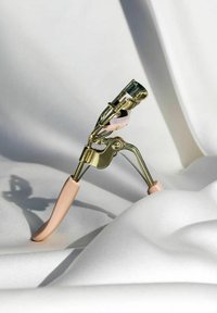 Recourbe-cils en or avec des poignées en caoutchouc rose, doté d'un coussin en silicone arrondi et d'un design compact et ergonomique sur fond blanc.