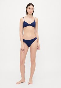 Navy blue bikini set featuring a triangle bra with thin straps and matching low-rise briefs. Smooth texture, minimal detailing.
