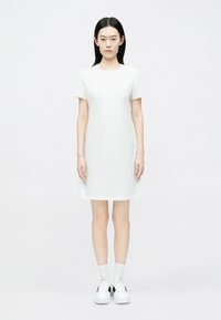 Valge lühikeste varrukatega kleit, ülaosas keha külge istuv, alt veidi lehvikujuline. Sile puuvillane kangas, põlvepikkune, kantud valgete sokkide ja vabaajajalatsitega.