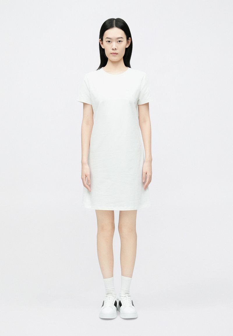 Valge lühikeste varrukatega kleit, ülaosas keha külge istuv, alt veidi lehvikujuline. Sile puuvillane kangas, põlvepikkune, kantud valgete sokkide ja vabaajajalatsitega.