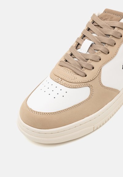 Beige lenkkari, jossa on valkoinen varvaskärki, valmistettu mokkaa ja nahkaa, pyöreät nauhat, rei'itetyt yksityiskohdat ja teksturoitu kumipohja.