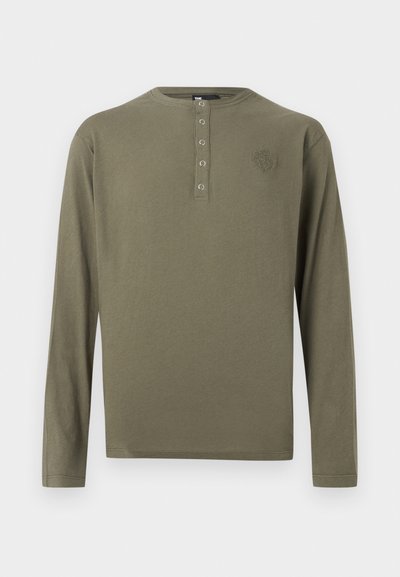 Olíva zöld hosszú ujjú henley ing négy fém patenttal és egy kis hímzett logóval a bal mellrészen.