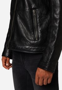 Zwarte leren jas met een glanzende afwerking, zijrits zak en gestikte details. Draag over donkere jeans, wat een mooie textuur laat zien.