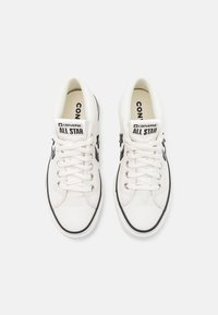 Para białych trampek Converse All Star z czarnym logo gwiazdy, sznurówki związane, widok z góry na jednolitym białym tle.