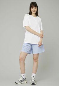 T-shirt blanc à manches courtes associé à des shorts rayés bleus et blancs. Le modèle porte des chaussures de sport argentées et des chaussettes blanches. Design simple, coupe décontractée.