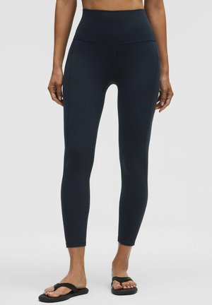 Granatowe legginsy z wysokim stanem wykonane z elastycznego, gładkiego materiału, z bocznymi panelami i dopasowanym krojem, zestawione z czarnymi klapkami.