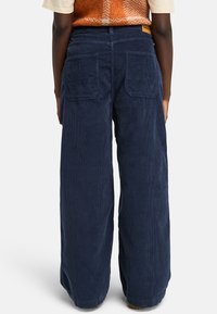 Pantalones de pana de corte ancho en color azul marino, con dos bolsillos traseros y un acabado texturizado. La cintura tiene una etiqueta de marca en la parte posterior.