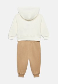 Ανοιχτόχρωμο κρεμ φούτερ με κουκούλα και ελαστικές μανσέτες, συνδυασμένο με ανοιχτό καφέ φόρμα με ελαστική μέση και μανσέτες.