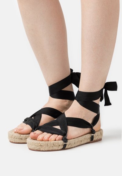 Μαύρες σαμπρέλες espadrille με σταυρωτές λουρίδες, πλατφόρμα με σκοινί και επίπεδη σόλα, με κορδόνια στον αστράγαλο για ασφαλή εφαρμογή.