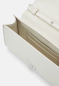 Billetera Calvin Klein en cuero beige claro, con textura suave, cierre a presión y compartimentos para tarjetas en el interior.