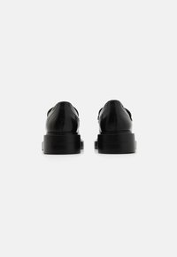 Scarpe nere in pelle con finitura liscia, punta tonda e suola in gomma nera spessa. Presentano un logo impressa sul tallone e un design minimalista.