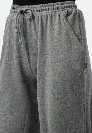 Pantaloni della tuta grigi con vita elastica e cordino, tasche laterali e un tessuto morbido e texturizzato. Piccola etichetta con il marchio di lato.