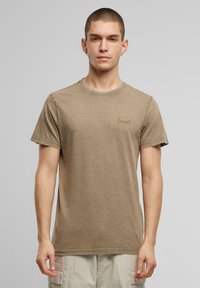 Brun bomulds t-shirt med rund halsudskæring, korte ærmer og en let tekstur. Har et diskret guld-logo på venstre bryst.